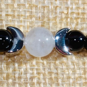 May include: A bracelet with black beads, a white bead, and silver crescent moon charms.