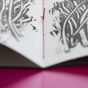 May include: A close-up of a book with a red thread binding. The pages are decorated with black and white leaf prints.