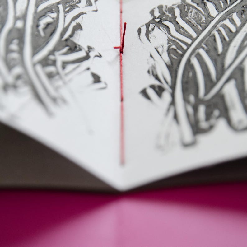May include: A close-up of a book with a red thread binding. The pages are decorated with black and white leaf prints.