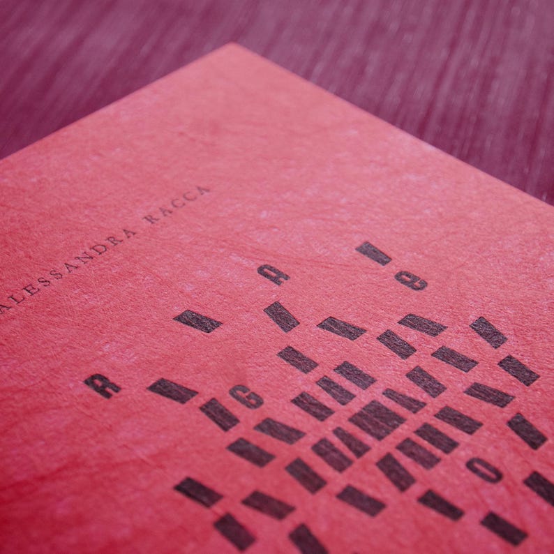 May include: A red book cover with the text "ALESSANDRA RACCA" printed in black. The cover features a pattern of black squares arranged in a geometric design.