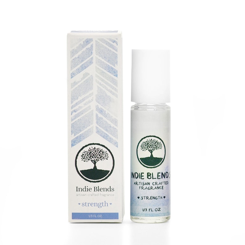 Puede incluir: Un frasco blanco de roll-on con un logotipo de &aacute;rbol verde y el texto "Indie Blends Artisan Crafted Fragrance Strength 1/3 FL OZ". El frasco est&aacute; al lado de una caja blanca con un patr&oacute;n azul y blanco y el texto "Indie Blends artisan crafted fragrance *strength* 1/3 FL OZ".