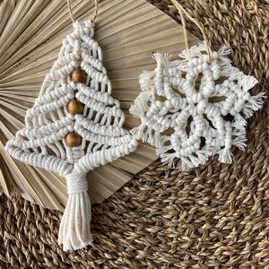 May include: Two handmade macrame ornaments, a white Christmas tree with wooden beads and a snowflake, on a woven background.
