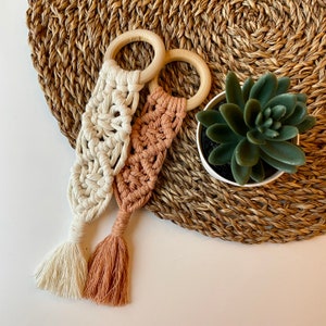 May include: Two crocheted baby teethers with wooden rings. One teether is white and the other is peach.