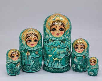 May include: A set of six teal nesting dolls, each with a painted face and a gold-colored headdress. The largest doll features a winter scene with figures and animals. The dolls are arranged in a row, showcasing their varying sizes and intricate designs.