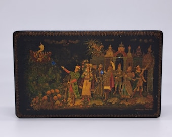 May include: A rectangular, black lacquered box with a detailed miniature painting. The painting shows figures in elaborate attire, with a boat in the background. The scene is set against a dark, detailed landscape.