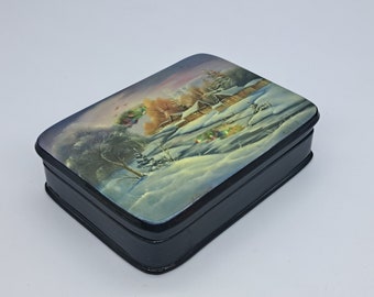 May include: A rectangular black box with a painted winter landscape scene on the lid. The artwork depicts a snow-covered village with houses, trees, and a colorful sky. The box has a glossy finish.
