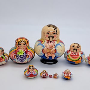 Può includere: Un set di otto bambole russe tradizionali, o bambole a incastro, dipinte con colori vivaci e motivi folcloristici. La bambola più grande raffigura un uomo che tiene un maiale, mentre le altre raffigurano donne e uomini in abiti tradizionali.