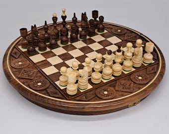 May include: A round wooden chess set with intricately carved detailing. The chess board features a checkerboard pattern with light and dark squares. The chess pieces are in light and dark brown tones, arranged for play.
