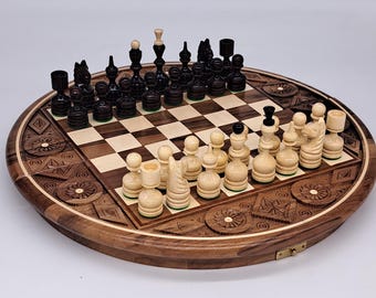 May include: A round wooden chess set with intricately carved border details. The chessboard features a light and dark square pattern, with black and white chess pieces arranged for play. The set is displayed on a white surface.
