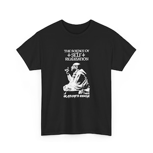May include: A black short-sleeve t-shirt featuring a white graphic print of a person sitting in profile. Above the figure is the text THE SCIENCE OF SELF REALIZATION with crosses, and below the figure is the text RAZOR'S EDGE.