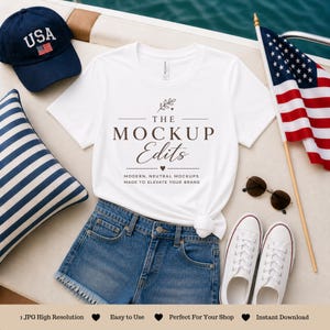 Könnte beinhalten: Ein weißes T-Shirt mit dem Text "THE MOCKUP Edits" wird mit Jeansshorts, weißen Turnschuhen und einer marineblauen "USA" Baseballkappe kombiniert. Eine amerikanische Flagge und Sonnenbrille vervollständigen die Szene, ideal für ein sommerliches Mockup.
