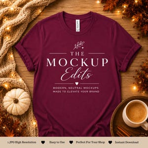 May include: A maroon short-sleeved t-shirt featuring white text that reads THE MOCKUP Edits, with the subtext MODERN, NEUTRAL MOCKUPS MADE TO ELEVATE YOUR BRAND, accompanied by a small leaf graphic and two small heart icons centered on the chest.