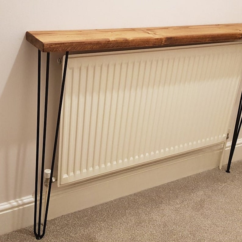 Op de afbeelding: Een houten plank met zwarte haarspeldpoten staat op een witte radiator. De plank is gemaakt van gerecycled hout en heeft een natuurlijke afwerking.