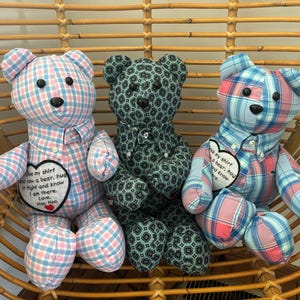 May include: Three stuffed bears made from patterned fabric. The left bear is pink and blue plaid, the center bear is dark green with a geometric pattern, and the right bear is blue and pink plaid. Each bear has black button eyes and a heart patch.