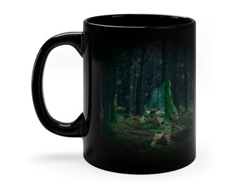 May include: Black ceramic mug featuring a forest scene with tall trees and a path. The image has a dark, moody aesthetic with green and brown tones. The mug has a curved handle.
