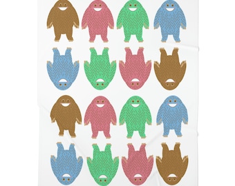 May include: A white blanket featuring a repeating pattern of smiling, furry monster illustrations. The monsters are in brown, pink, green, and blue, alternating between upright and upside-down orientations. The blanket is a soft, cozy home decor item.