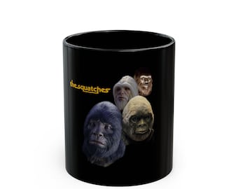 May include: A black ceramic mug featuring a graphic of five different primate-like faces arranged in a cluster. To the left of the faces, the text "the squatches" is printed in a bold, yellow, sans-serif font against the solid black background.