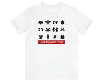 May include: White t-shirt featuring a series of black inkblot designs, arranged in rows. Below the images is a red rectangular banner with the text "Rorsquatch Test" in white. The shirt is a casual wear item.