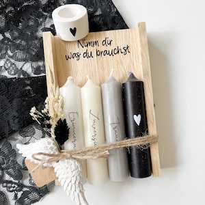 May include: A wooden box with four candles, each with a different inscription: "Traume", "Zuerst", "Erinnern", and "Nimm dir was du brauchst". The box also includes a small white ceramic candle holder with a heart.