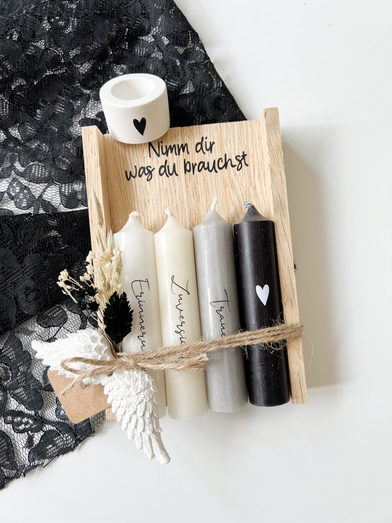 May include: A wooden box with four candles, each with a different inscription: "Traume", "Zuerst", "Erinnern", and "Nimm dir was du brauchst". The box also includes a small white ceramic candle holder with a heart.