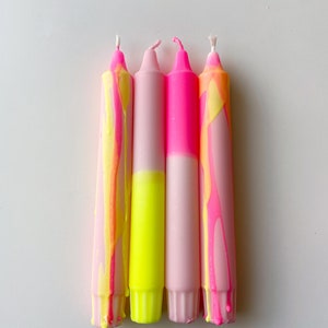May include: Four pink and yellow candles with a marbled design. The candles are arranged in a row, with the pink portion of each candle facing the viewer.
