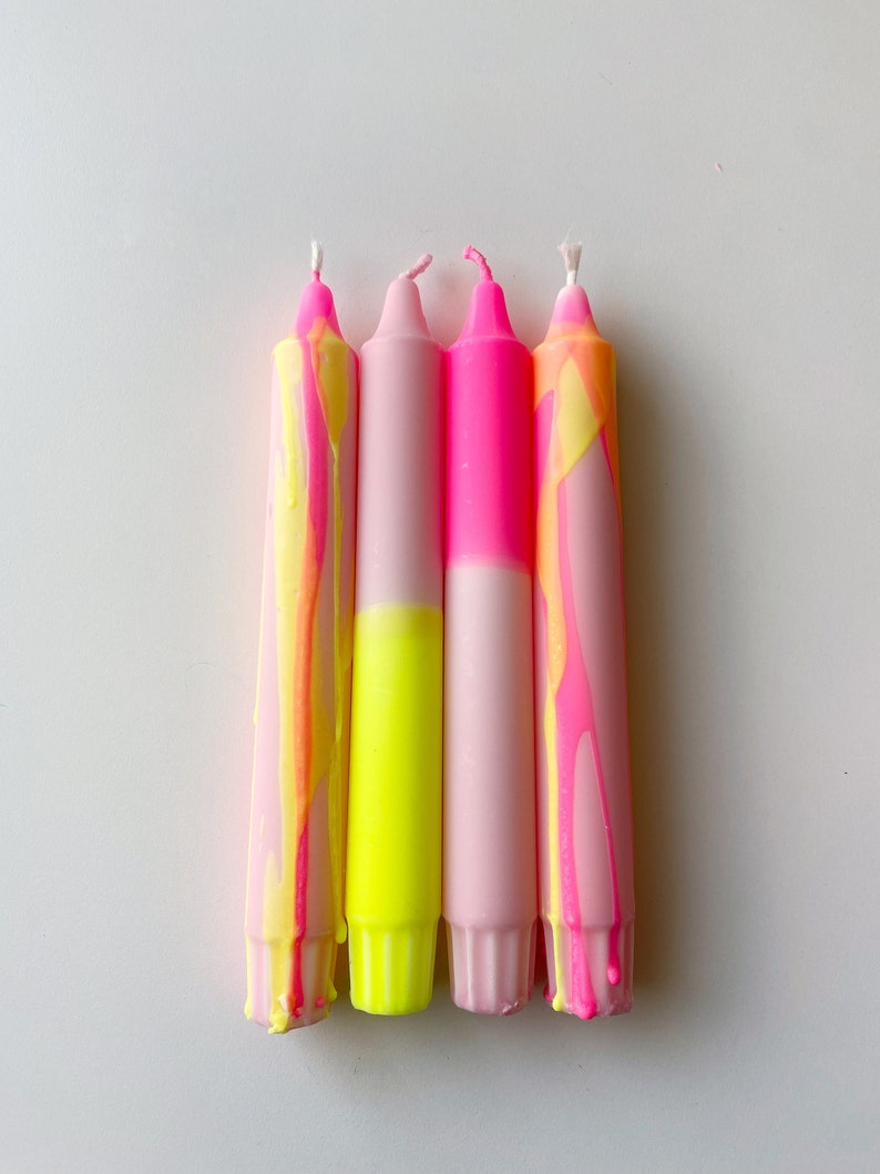 May include: Four pink and yellow candles with a marbled design. The candles are arranged in a row, with the pink portion of each candle facing the viewer.
