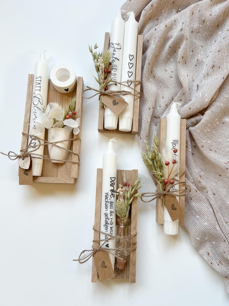 May include: Four wooden boxes with candles and dried flowers. The candles are white and have text on them. The boxes are tied with twine and have small tags with hearts on them. The text on the candles reads "Danke, dass du mir beim Wachsen geholfen hast", "Janke HDMI", "We", and "STATT Blumen".