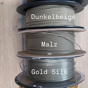May include: A stack of five spools of 3D printing filament in various colors. The colors include brown, dark beige, malz, gold silk, and gold. Each spool is labeled with its color name.
