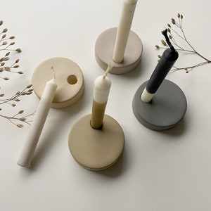 Peut inclure: Quatre bougeoirs en céramique beige, gris et brun clair avec des bougies blanches, noires et beiges. Les bougeoirs sont ronds et ont un petit trou au centre pour que la bougie puisse s'y asseoir.