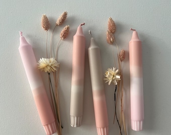 Könnte beinhalten: Fünf Ombre-Kerzen in Rosa- und Beigetönen. Die Kerzen sind in einer Reihe angeordnet und von Trockenblumen umgeben.