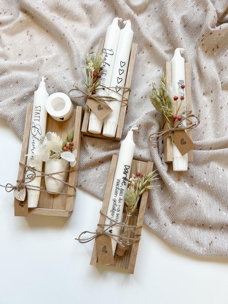 May include: Three wooden boxes with candles and dried flowers. The candles are white and have text on them. The boxes are tied with twine and have a small tag with a heart on it. The text on the candles reads "Danke, dass du mir beim Wachsen geholfen hast", "Statt Blumen" and "Janke HD M".