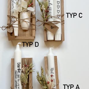 May include: Four different types of wooden candle holders with white candles. Each holder has a small bouquet of dried flowers and a tag with a handwritten message. The messages are "STATT Blumin", "Jaunke HID ALIK", "Danke, dass du mir beim Wachsen geholfen hat", and "Weil du da bist".