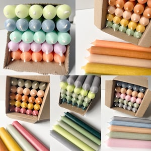 Puede incluir: Surtido de velas de té de colores en varios tonos de verde, azul, rosa, naranja y amarillo. Las velas están dispuestas en cajas y sobre una mesa.