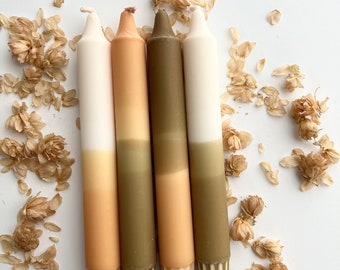 May include: Four ombre taper candles with a white, beige, and green color scheme. The candles are arranged in a row and are surrounded by dried flower petals.