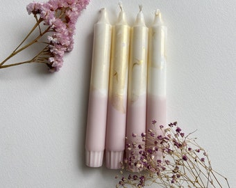 Könnte beinhalten: Vier rosa und weiße Kerzen mit goldenen Akzenten. Die Kerzen sind in einer Reihe angeordnet und haben eine rosa Basis und eine weiße Spitze mit goldenen Flocken.
