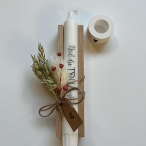 May include: A white candle with the text "Weil du Toll bist" on it, in a wooden holder with a small bouquet of dried flowers and a brown tag with a heart on it.