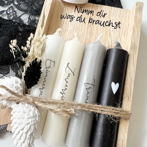 May include: A wooden box with four candles, each with a different inscription: "Erinnerung", "Zweifel", "Traum", and a heart. The box also has a small white candle holder with a heart on it and the text "Nimm dir was du brauchst".