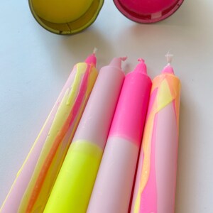 May include: Four candles with pink and yellow marbled wax. Two candles are pink with a white base and two candles are yellow with a pink base.
