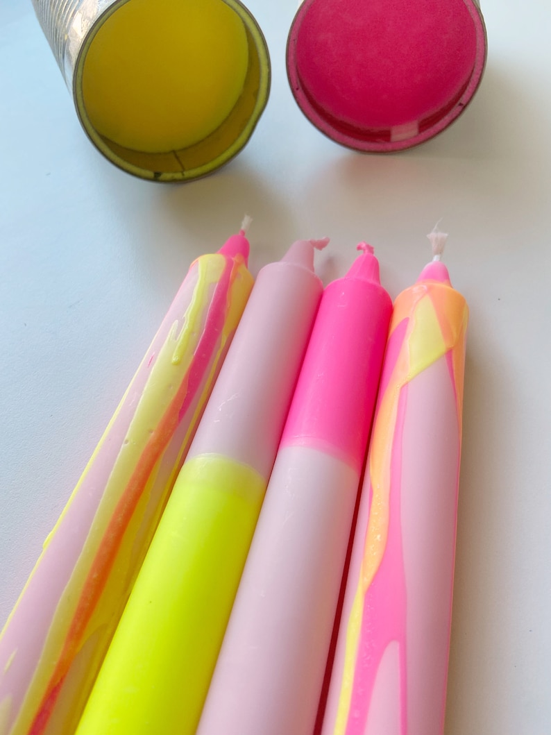 May include: Four candles with pink and yellow marbled wax. Two candles are pink with a white base and two candles are yellow with a pink base.
