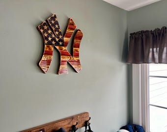 May include: A wooden New York Yankees logo painted with the American flag colors. The logo is mounted on a wall.