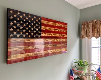 May include: A wooden American flag wall art with red, white, and blue colors. The flag is made of individual wood planks and has a distressed look. The stars are gold and the stripes are a mix of red and brown.