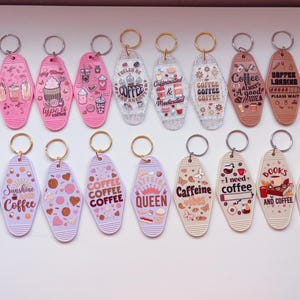 May include: A collection of retro-style keychains in various colors, featuring coffee-themed designs and phrases like "But First Coffee" and "Good Vibes Only." Each keychain has a metal ring.
