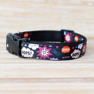 May include: Black dog collar with a repeating pattern of comic book style speech bubbles and starbursts in pink, orange, and white. The collar has a black plastic buckle and the text "OOPS!", "OMG!", "SUPER!", and "WOW".