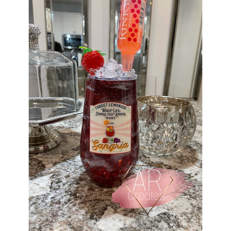 May include: Red glitter tumbler with a white sticker that says "Forget Lemonade When Life Hands You Lemons - Make Sangria". The sticker has a picture of a glass of sangria with fruit. A red and white straw is in the tumbler.