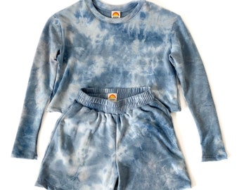 May include: A blue tie-dye long-sleeve shirt and matching shorts set. The shirt has a crew neck and the shorts have an elastic waistband.
