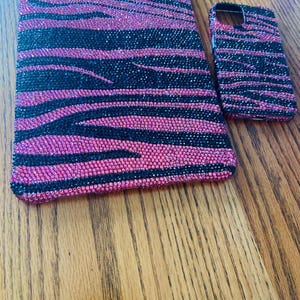 Könnte beinhalten: Ein pinkfarbenes und schwarzes Handy-Case mit Zebra-Muster und ein passendes Tablet-Case. Beide Cases sind mit Strasssteinen besetzt.