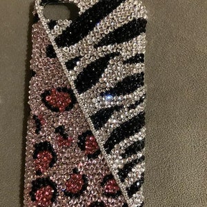 May include: A black and white zebra print phone case with a pink and red leopard print design. The case is covered in rhinestones.