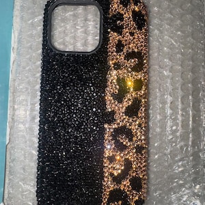 Op de afbeelding: Een zwarte telefoonhoes met een gouden en zwarte luipaardprint. De hoes is bedekt met strass.