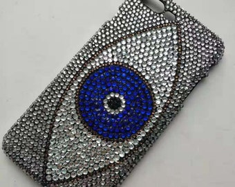 May include: A black phone case covered in clear and blue rhinestones, forming the shape of an evil eye.