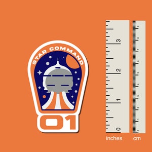 May include: A white sticker with a blue and orange space-themed design. The sticker features a spaceship, stars, and the text "STAR COMMAND 01".